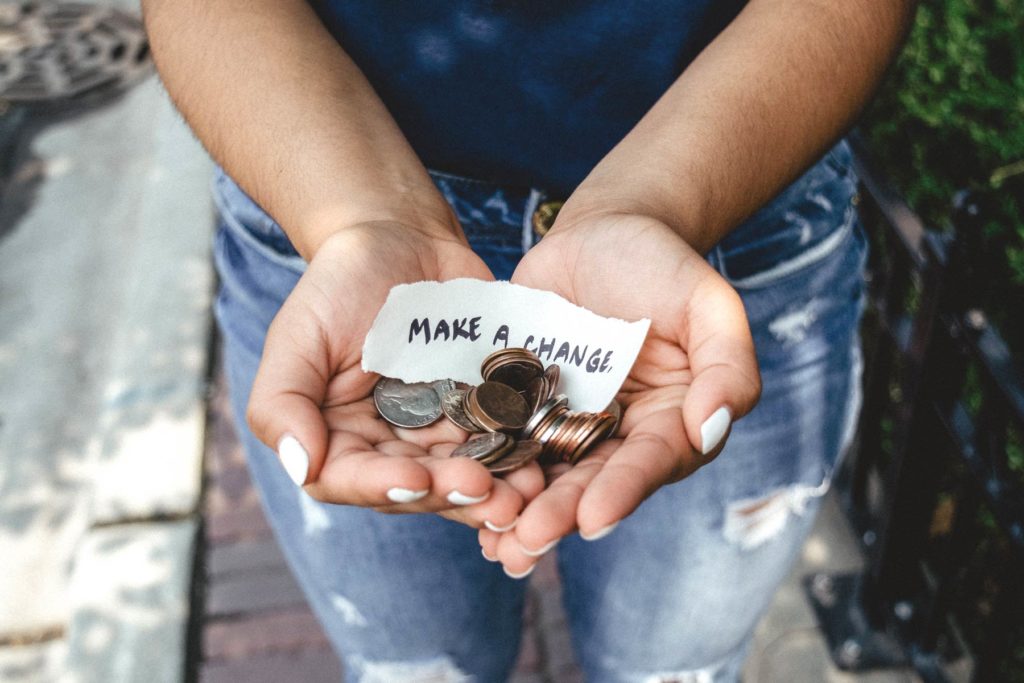 Person holding their hands outstreched, holding change and scrap of paper that says "make a change". Photo by Kat Yukawa